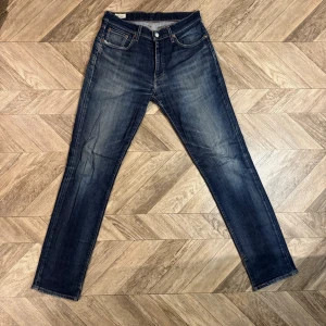 Mörkblå 511 Levi's  - Snygga mörkblå jeans med raka ben och diskreta slitningar på framsidan. Klassisk femficksmodell med knappgylf och kontrastsömmar. Jeansen har en tidlös tvätt och passar perfekt till en avslappnad stil. Materialet är denim i bomull.