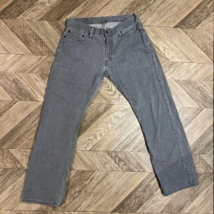 Gråa 514 Levi's  - Säljer ett par grå jeans med rak passform och klassisk femficksdesign. Jeansen har bälteshällor, knappgylf och synliga sömmar. Perfekta för en avslappnad och stilren look.