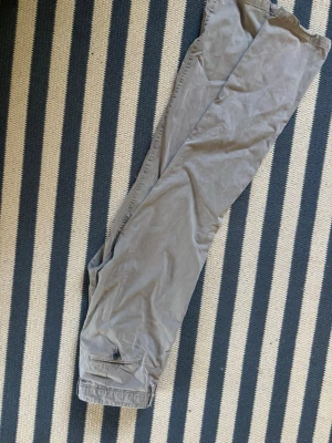 Gråa raka Calvin Klein byxor  - Snygga grå med rak passform och klassiska fickor fram och bak. Byxorna har bälteshällor och stängs med knapp och dragkedja. Perfekta för dig som gillar en avslappnad men stilren look.