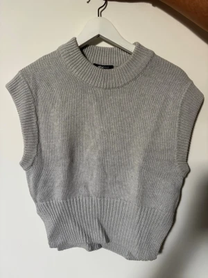 Grå stickad väst Gina Tricot - Grå stickad väst från Gina Tricot med bred ribbad kant nedtill och vid halsen. Ärmlös modell med hög krage och mjukt, tjockt material. Perfekt att bära över en skjorta eller t-shirt för en trendig lager-på-lager-look.
