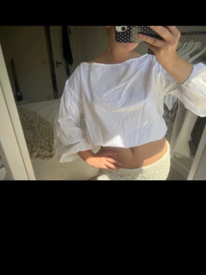 Vit croppad blus med vida ärmar - Trendig vit blus med vida långärmar och rund halsringning. Tillverkad i ett lätt bomullsliknande material som ger en luftig känsla. Perfekt att styla med höga jeans eller kjol för en fräsch look.