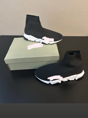 Svarta sock sneakers med vit sula - Säljer ett par svarta sock sneakers med stretchigt stickat material och vit chunky sula. Skorna har en strumpliknande design som sitter tight runt ankeln och ger en modern look. Perfekta för dig som gillar streetwear och vill ha något bekvämt och stilrent.