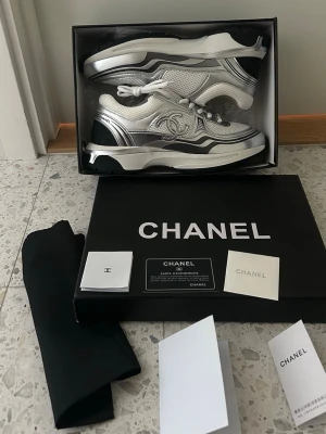 Chanel Runners silver/vit/svart - Säljer ett par exklusiva Chanel sneakers i silver, vitt och svart. Riktigt unika och feta passar till allt. Box, dustbag och tags medföljer. Fraktar inom 1 dag!