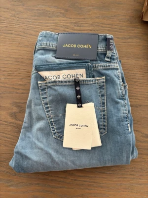 Jacob Cohen jeans - Hei. Selger dette helt nye paret med Jacob Cohen jeans. Veldig fin lys vask på disse Nypris 5900kr Min pris 3215kr Selges pga jeg tenker å kjøpe noe annet     Fra Jacob Cohen: Low waist Slim fit Knapper i gylf Skinnpatch på linning bak Vevd tørkle og trådsnelle følger med  Dette produktet er produsert for hånd i Italia, og parfymert med Jacob Cohën sin anerkjente duft  72% Bomull, 14% Viskose, 12% Polyester, 2% Elastan   Ai: Blå Jacob Cohën Bard jeans i denim, str M / W31, normal i størrelsen. K
