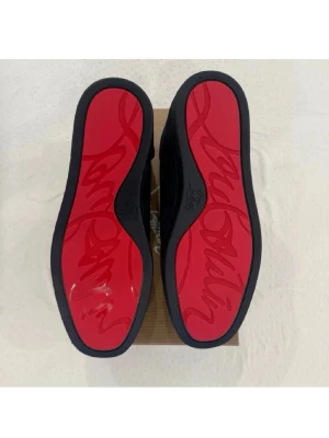 Mörkblå sneakers med röd sula - Snygga mörkblå sneakers i mocka med klassisk låg profil och matchande blå skosnören. Skorna har en ikonisk röd sula med grafiskt mönster undertill och beige innerfoder. Perfekta för dig som vill sticka ut med stilrena detaljer.