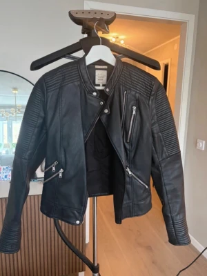 Svart biker skinnjacka med dragkedjor - Snygg svart skinnjacka i bikerstil med detaljerade sömmar på axlar och ärmar. Från Zara storlek XS, lite slitage på insidan av nacken se sista bilden