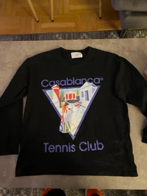 Svart långärmad topp Casablanca - Säljer en svart långärmad topp från Casablanca med färgglatt tryck och texten 'Tennis Club' på framsidan. Toppen har en avslappnad passform och är perfekt för dig som gillar streetwear och grafiska prints.