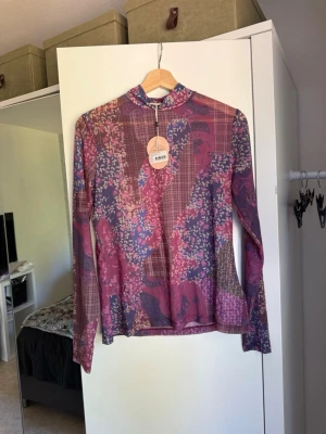 Mönstrad mesh polotopp Odd Molly - Säljer en tunn och stretchig mesh polotopp från Odd Molly. Toppen har ett färgstarkt mönster i lila, rosa och blå toner med blommiga och rutiga inslag. Långärmad och figurnära passform, perfekt för att lyfta vilken outfit som helst. Från märket Odd Molly i storlek 3 som enligt deras storlekguide motsvarar en storlek L. Helt ny med tags/ prislapp fortfarande kvar. 