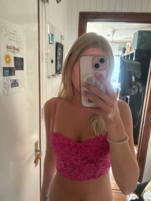 Rosa spetsig korsettopp från New Yorker  - Säljer en snygg rosa korsettopp från New Yorker i storlek XS. Toppen är croppad och har tunna axelband samt är tillverkad i spets med blommigt mönster. Perfekt för dig som vill ha en statement piece till sommaren.