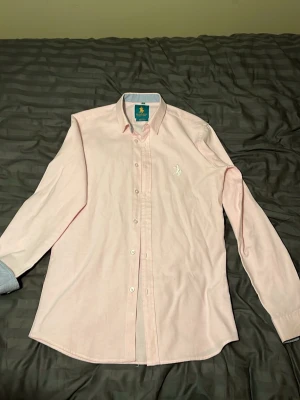 Ljusrosa skjorta från Beverly Hills Polo Club - Snygg ljusrosa skjorta från Beverly Hills Polo Club med slim fit-passform. Skjortan har klassisk krage, långa ärmar och vit broderad logga på bröstet. Tillverkad i mjukt bomullstyg och har vita knappar framtill.