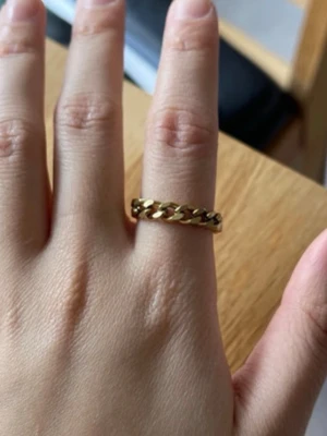 Guldfärgad kedjering - Snygg guldfärgad ring med kedjedesign. Ringen har en chunky look och är tillverkad i metall med blank finish. Perfekt för dig som gillar trendiga accessoarer och vill addera lite edge till din stil.