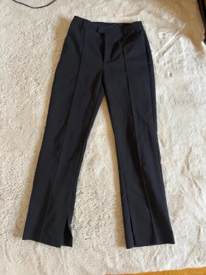 Svarta kostymbyxor med pressveck - Snygga svarta kostymbyxor med raka ben och markerade pressveck framtill. Byxorna har en klassisk midja och diskreta fickor. Materialet ser ut att vara en blandning av polyester och viskos för en dressad look.
