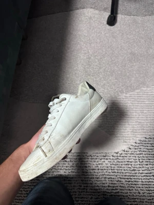 Vita sneakers med svart detalj - Stilrena vita sneakers med svart detalj på hälen. Skorna har klassisk låg profil, vita snören och sula. Tillverkade i slätt material som ger en clean look. Perfekta för dig som gillar minimalistisk stil.