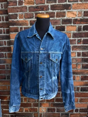 Levi’s 70500-0401 Trucker Jeansjacka XL 100% Bomull - Snygg blå jeansjacka i klassisk modell med raka linjer och två bröstfickor med knapp. Jackan har silverfärgade knappar framtill och på fickorna samt en tidlös tvättad denimlook. Perfekt att slänga över en hoodie eller t-shirt för en avslappnad stil.
