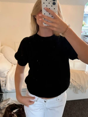 Svart croppad stickad topp - Säljer en svart croppad stickad topp med korta ärmar och rund hals. Toppen har en enkel och stilren design som passar perfekt till både jeans och kjol. Materialet är mjukt och bekvämt, vilket gör den skön att bära hela dagen.