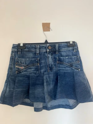 Blå jeanskjol med volang - Säljer en kort blå jeanskjol med bred volangkant. Äkta disel och i storlek XXS/XS.