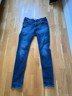 Mörkblå slim fit jeans - Säljer ett par mörkblå slim fit jeans med klassisk femficksdesign och lätt slitna detaljer på framsidan. Jeansen har normal midja och raka ben, perfekta för en avslappnad men ändå snygg look.