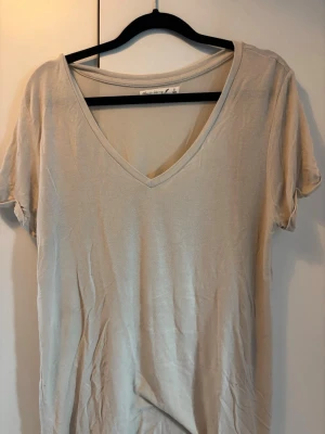 Beige v-ringad t-shirt Black Story - Säljer en enkel och stilren beige t-shirt från Black Story i storlek S. T-shirten har v-ringning och korta ärmar, perfekt för en avslappnad look. Tillverkad i mjuk bomull som känns skön mot huden.