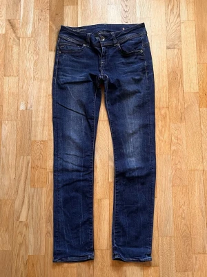 Gstar midge raw 29/32 wmn  - Snygga mörkblå jeans med klassisk femficksdesign och kontrastsömmar. Jeansen har en något tvättad look med subtila slitningar och raka ben. Perfekta för dig som gillar en enkel men stilren stil.