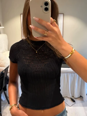 Svart Zara topp - Säljer en svart topp med korta ärmar och ett spets håligt liknande mönster. Toppen är figurnära och har en rund halsringning. Perfekt att styla med jeans eller kjol för en trendig look. Gammal från Zara