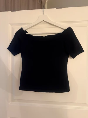 Svart offshoulder topp från H&M - Säljer en svart offshoulder topp från H&M. Toppen har korta ärmar och en tight passform som framhäver figuren. Perfekt att styla med jeans eller kjol för en trendig look.