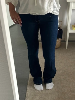 Mörkblå bootcut jeans - Säljer ett par mörkblå bootcut jeans med klassisk femficksdesign och hög midja. Jeansen har en snygg, figurnära passform upptill och lätt utsvängda ben. Perfekta till en avslappnad men ändå trendig look.