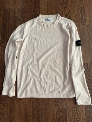 Beige långärmad tröja Stone Island - Snygg beige långärmad tröja från Stone Island med klassisk patch på ärmen. Tröjan har rund halsringning och är tillverkad i mjukt material som känns skönt mot huden. Perfekt för dig som gillar stilrena och tidlösa plagg.