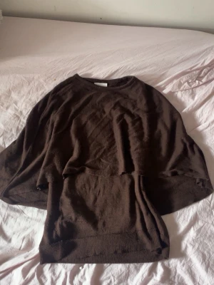Brun stickad poncho från H&M - Mysig brun stickad poncho från H&M med rund halsringning och avslappnad passform. Perfekt att slänga över en t-shirt eller långärmad tröja för extra värme. Tillverkad i mjukt material som känns skönt mot huden.