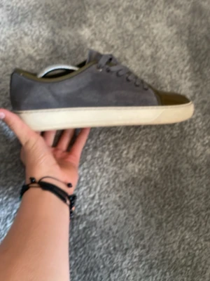 Lanvins - Säljer ett par stilrena sneakers i grå mocka med olivgrön tå i blankt material och matchande detaljer. Skorna har snörning och vit sula, perfekta för dig som vill ha en unik touch på din outfit. Lanvins till mycket billigt pris, priset går o diskuteras vid snabb affär!