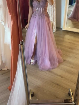 Lila långklänning med slits och pärlor - Bild från hon jag köpte av😇. Lila långklänning med glittriga pärldetaljer upptill och markerad midja. Klänningen har en djup v-ringning, smala axelband och en hög slits framtill. Kjolen är i flera lager tyll för extra volym. Använd 1 gång, fråga för fler bilder och kom gärna med bud💞