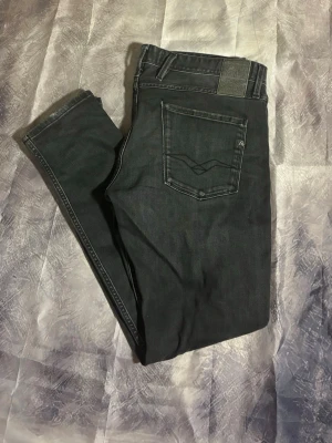 Svarta slim fit jeans - Säljer ett par svarta slim fit jeans med klassisk femficksdesign och diskreta sömmar på bakfickorna. Jeansen har normal midja och smala ben. Materialet känns mjukt och stretchigt, perfekt för en avslappnad look.