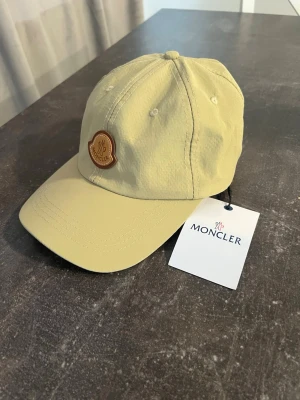 Moncler Keps - Säljer denna keps från Moncler. Aldrig använd och har även lappen kvar. En fin beige färg som är mer sällsynt att hitta. Vid eventuella frågor eller funderingar, skriv!