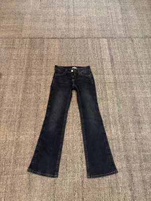 Mörkblå bootcut jeans med brodyr - Snygga mörkblå bootcut jeans med kontrastsömmar och broderade detaljer på bakfickorna. Klassisk femficksmodell och knappgylf.