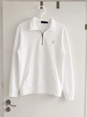Vit halfzip hoodie från Polo Ralph Lauren - Polo Ralph Lauren Half-Zip Sweatshirt – Vit – Som ny  Säljer en stilren och tidlös half-zip sweatshirt från Polo Ralph Lauren i klassisk vit färg. Tröjan är i nyskick och har inga tecken på användning. Köpt i herrmodell för att få en snygg oversized-passform.  Detaljer: 	•	Märke: Polo Ralph Lauren 	•	Storlek: Herr S (motsvarar ungefär dam M för en oversized passform) 	•	Färg: Vit 	•	Half-zip med hög krage 	•	Broderad Ralph Lauren-logga på bröstet 	•	Känguruficka framtill 	•	Skick: Som ny 