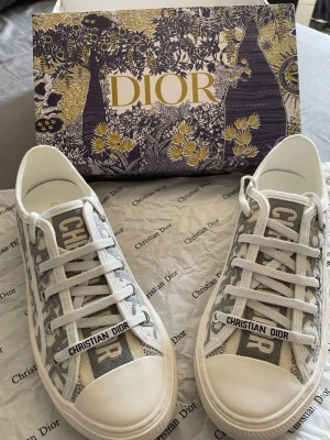 Christian Dior gråvita sneakers - Snygga sneakers från Christian Dior i grått och vit. Skorna är i jättebra skick och är normala till storleken, och så sjuktttt fina!!. Perfekta för dig som vill ha en exklusiv och trendig look.