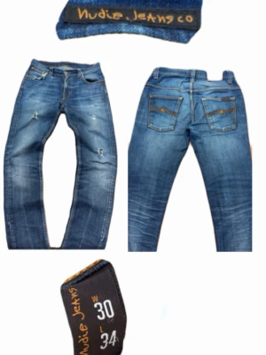 Nudie Jeans - Säljer ett par blå jeans från Nudie Jeans med slitningar och tvättade detaljer. Modellen har raka ben, klassiska fem fickor och orange sömmar på bakfickorna. Perfekta för en avslappnad och trendig look.