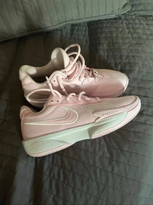 Nike G.T. Cut Academy rosa sneakers - Säljer ett par ljusrosa Nike G.T. Cut Academy sneakers med vit sula och mesh-överdel. Skorna har tydlig Nike-logga på sidan och texten 'G.T. Cut academy' på plösen. Perfekta för basket eller träning, med snygg sportig design och bra komfort. Endast använda ett fåtal gånger, är i extremt bra skick! Köpta för 1500 då de är egendesignade.