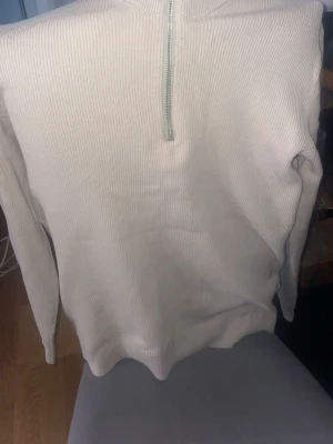 Beige stickad tröja jack&jones  - Stickad tröja i beige från Only & Sons med ribbad struktur och halv dragkedja framtill. Tröjan har lång ärm och hög krage, perfekt för lager på lager. Enkel och stilren design som passar till det mesta.