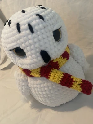 Virkad uggla med Gryffindor-halsduk - Supergullig virkad uggla i mjukt vitt garn med stora gula ögon och broderade detaljer. Ugglan har en stickad halsduk i rött och gult, inspirerad av Gryffindor från Harry Potter. Perfekt som accessoar eller dekoration till rummet. 20 cm 
