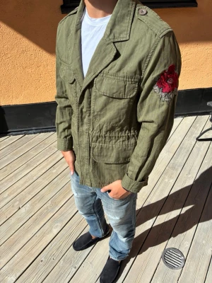 Olivgrön overshirt med broderad ros - Sjukt snygg overshirt, storlek s men passar som m. Bra skick skriv vid frågor eller funderingar och följ för mer!