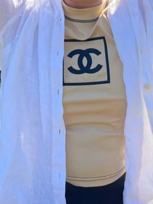 Beige ärmlös topp från cc  - Snygg beige ärmlös topp från cc med svart logga framtill. Toppen har svarta kontrastsömmar och en högre rund halsringning. Tyger slätas ut när du bär den supercool i STL S köpt i Milano för 2500 sek på en vintage butik . 