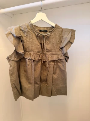 Grön blus med volang  - Snygg grön blus med volangdetaljer på axlarna och knytband vid halsen. Blusen har en lös passform, rund halsringning och fina veckade detaljer framtill. Tillverkad i ett lätt bomullsliknande material som känns luftigt och bekvämt.
