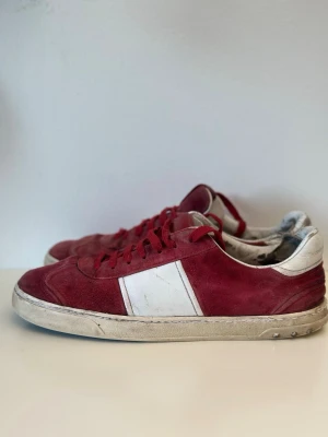 Röda och vita sneakers i mocka - Snygga sneakers i röd mocka med vita detaljer och vit sula. Skorna har en klassisk låg profil och vita partier på sidan samt vid hälen. Yttermaterialet är mocka och de har röda skosnören. Perfekta för dig som gillar retrostil och vill sticka ut.