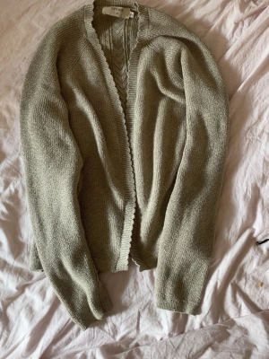 Beige/guld stickad kofta från Cream - Säljer en beige/guld stickad kofta från & Other Stories. Koftan har lång ärm, öppen framtill och fina vågiga kanter längs öppningen. Materialet känns mjukt och lätt, perfekt för lager på lager. Enkel och stilren design som passar till mycket.