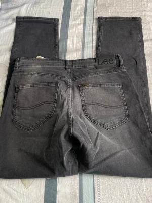 Grå jeans från Lee med raka ben - Säljer ett par grå jeans från Lee med klassisk femficksmodell och raka ben. Jeansen har Lee-logga på bakfickan och är tillverkade i mjukt denimtyg. Perfekta för en avslappnad och stilren look.