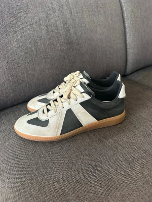 Oreo Gats - Snygga sneakers i svart och beige med klassisk låg profil och kontrasterande detaljer. Skorna har beige snörning och en slitstark gummisula med bra grepp. Materialet ser ut att vara en mix av mocka och textil, perfekt för en avslappnad streetstyle.