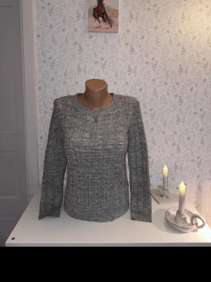 Grå stickad tröja med rund hals - En enkel och stilren grå stickad tröja med rund halsringning och långa ärmar. Tröjan har en diskret ribbad struktur och är perfekt för lager på lager. Passar till både jeans och kjol för en avslappnad look. ”Köpt begagnat. Jättefin men tyvärr var för liten för mig.”