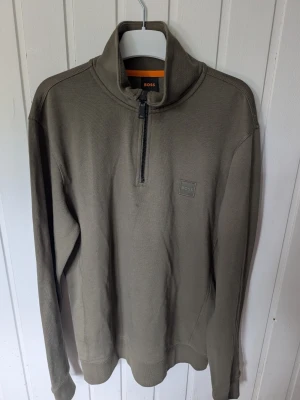 Olivgrön halfzip tröja från BOSS - Snygg olivgrön tröja från BOSS med halv dragkedja och hög krage. Tröjan har en diskret BOSS-logga på bröstet och är tillverkad i mjukt material. Perfekt för lager på lager och enkel att matcha med jeans eller chinos.