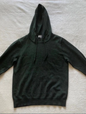 Mörkgrön hoodie med huva - En stilren mörkgrön hoodie med huva och dragsnören. Hoodien har långa ärmar, ribbade muddar vid ärmslut och nederkant samt en mjuk, stickad känsla. Perfekt för dig som gillar en enkel och clean look.