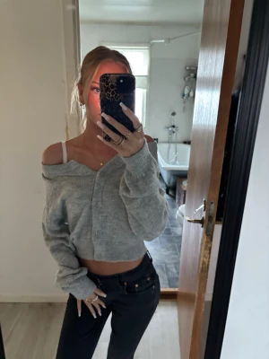 Grå croppad kofta - Säljer en ljusgrå croppad kofta med knappar framtill. Koftan har en avslappnad passform och långa ärmar, perfekt att bära off-shoulder för en trendig look. Mjuk och skön, passar till jeans eller kjol.